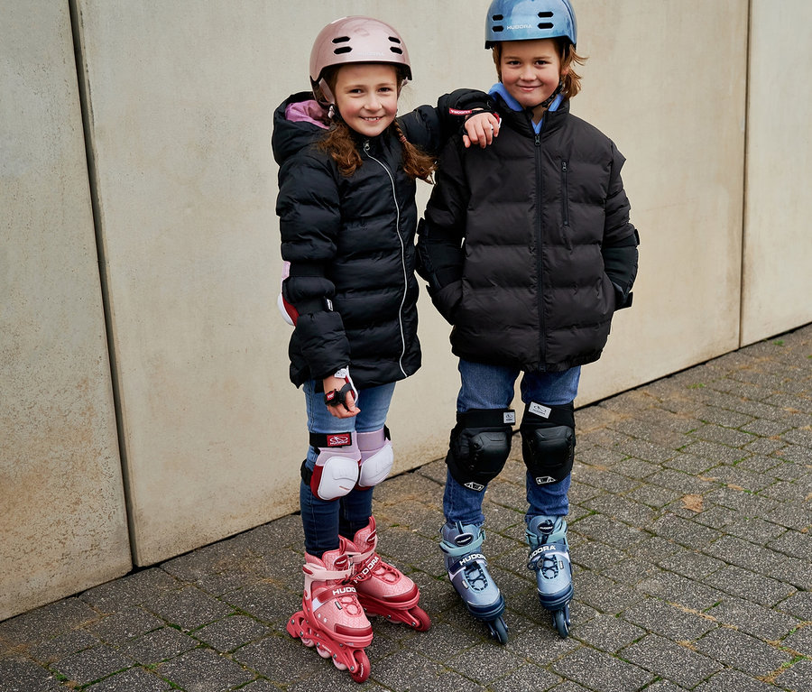 Zwei Kinder mit Helmen und Schützern stehen nebeneinander auf HUDORA Inline Skates »Mia 2.0« und HUDORA Inline Skates »Leon 2.0«.