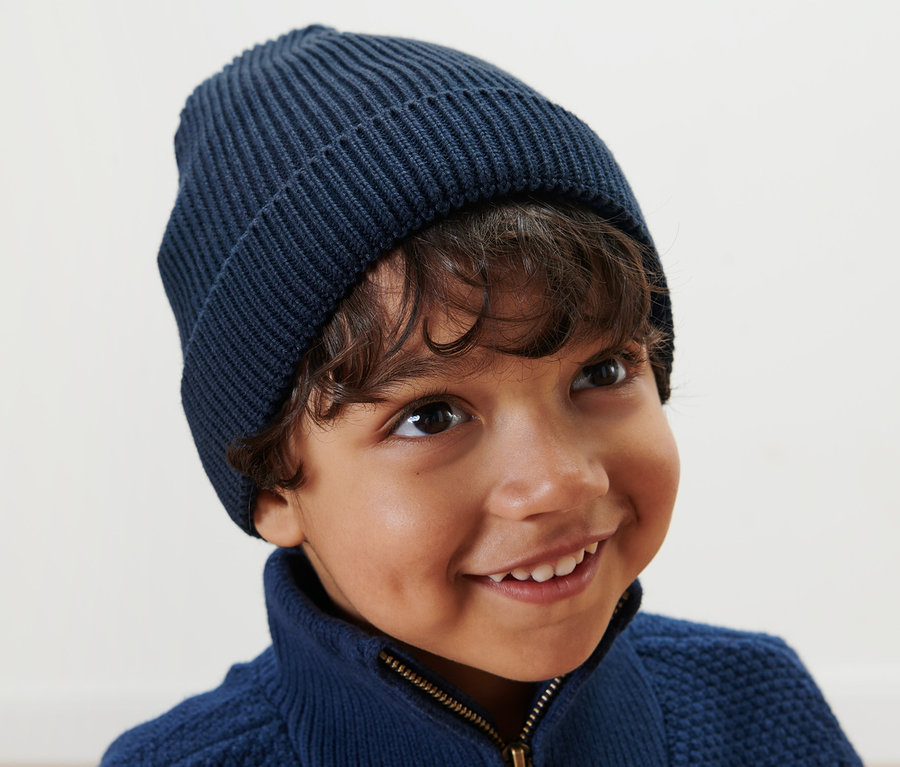 Lächelnder Junge trägt eine blaue Kinder-Strickmütze.