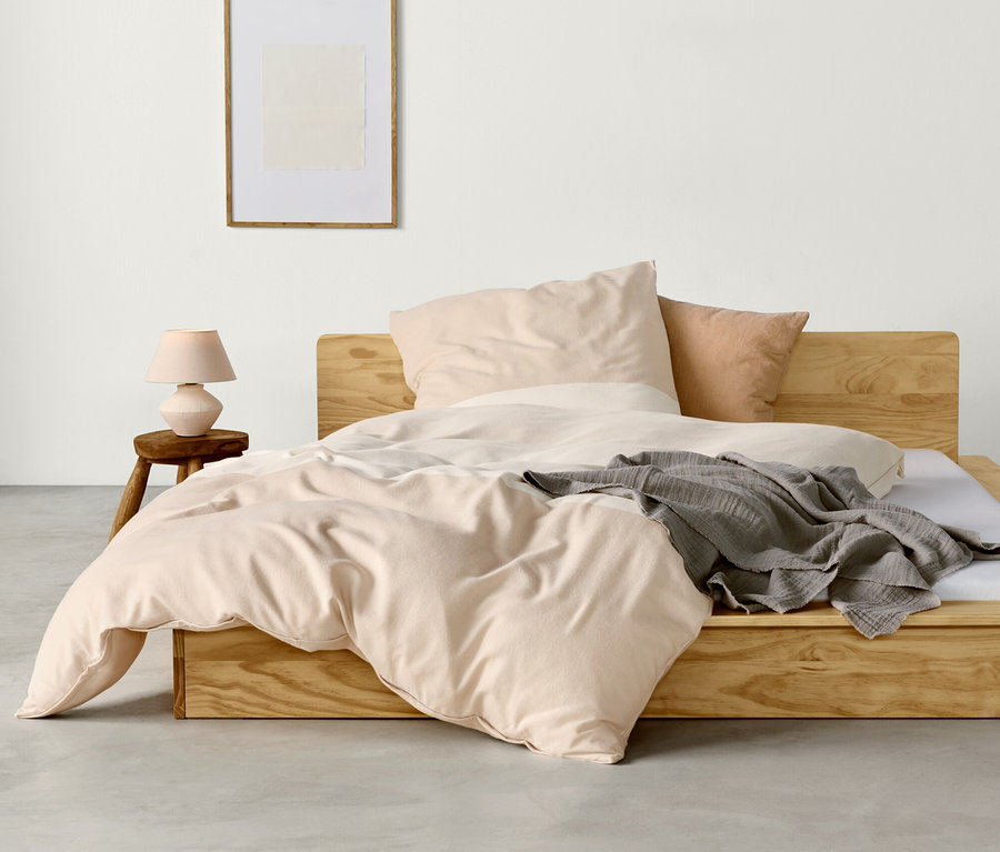 Schlafzimmer mit Holzbett, beige Flanell-Bettwäsche in Normal- und Übergröße und grauer Decke.