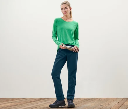 Frau im grünen Shirt hält eine silberne Flasche und trägt eine Softshellhose.