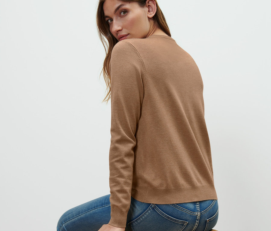 Frau sitzt auf einem Holzhocker und trägt einen Feinstrick-Cardigan.