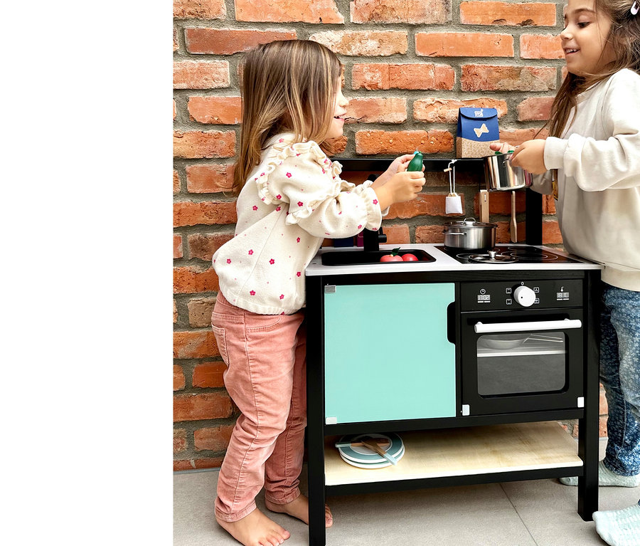 Zwei Mädchen spielen mit der small foot Kinderküche »Industrial« vor einer Ziegelwand.