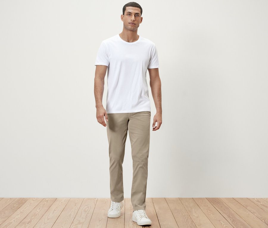 Mann steht in weißem T-Shirt und beiger Chino.