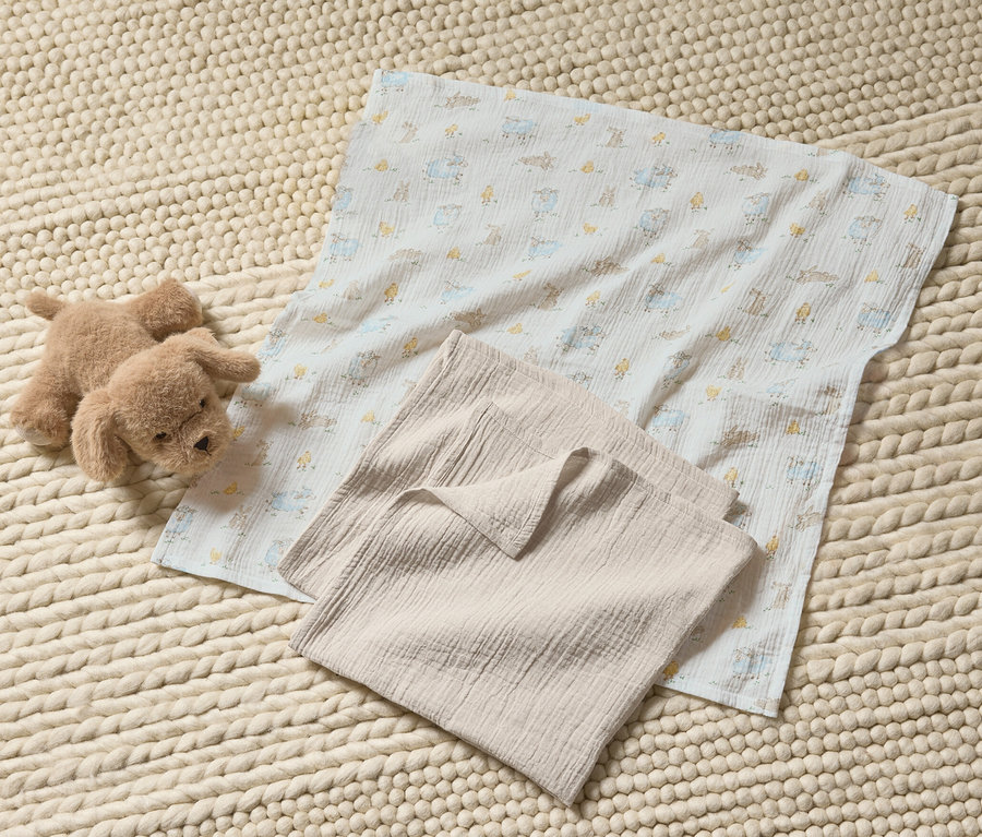 Ein Stofftier-Hund und 3 Baby-Musselin-Tücher auf einem gestrickten Teppich.