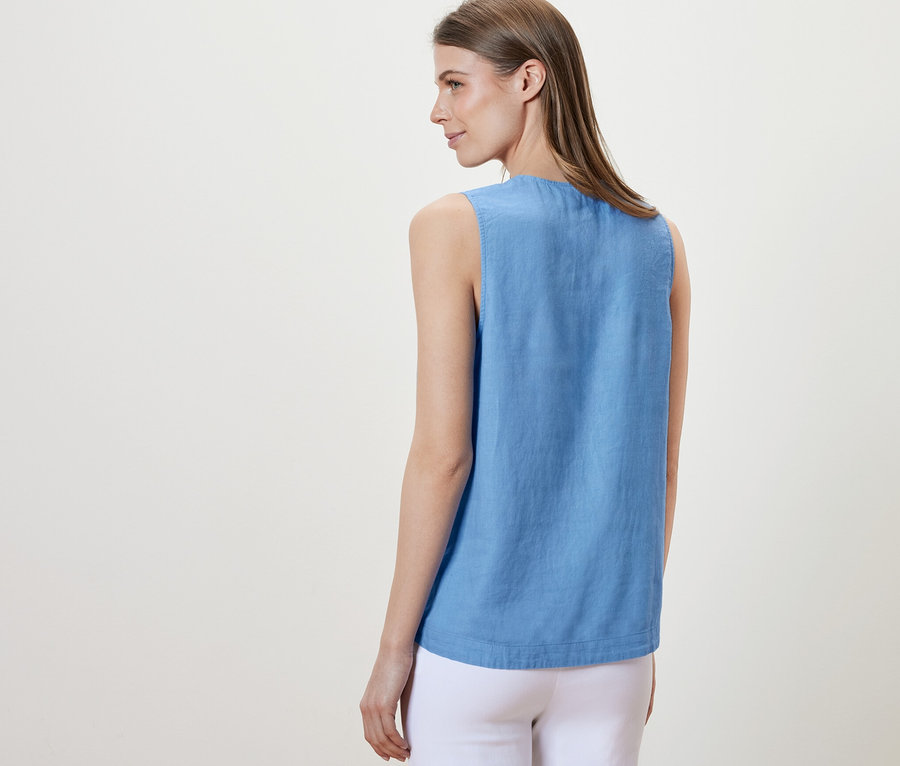 Frau steht mit dem Rücken zur Kamera und trägt eine hellblaue, ärmellose Leinenbluse.