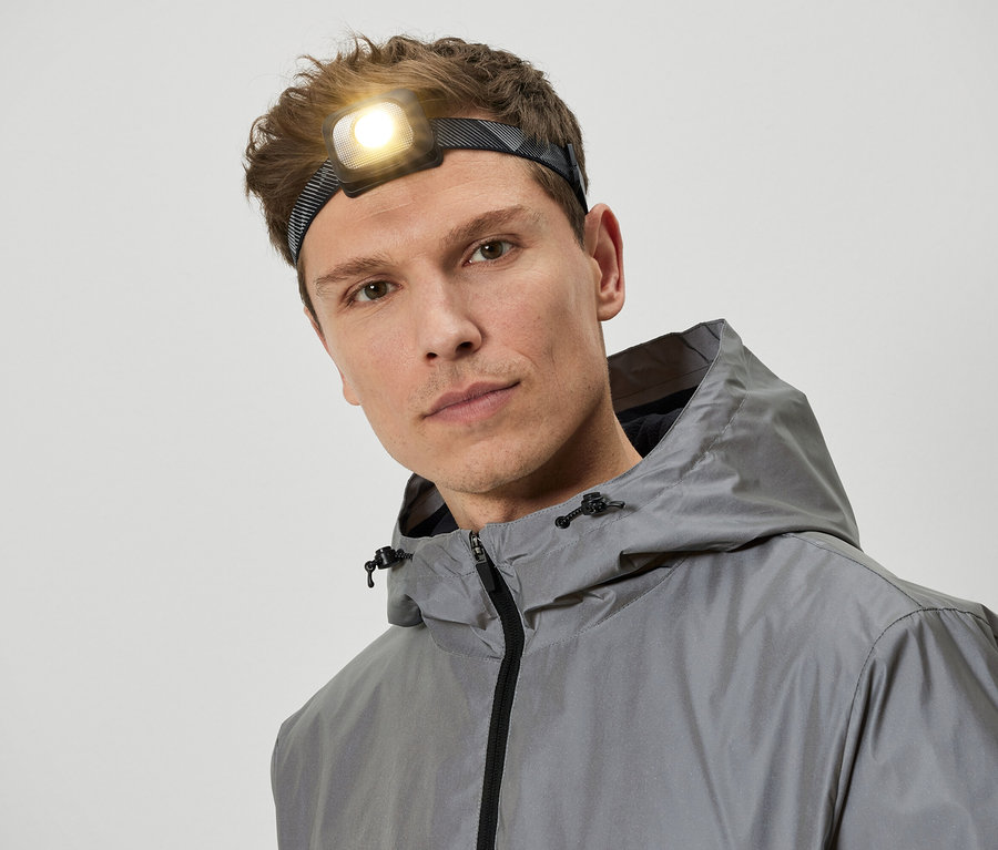 Mann mit Stirnlampe und grauer Kapuzenjacke.