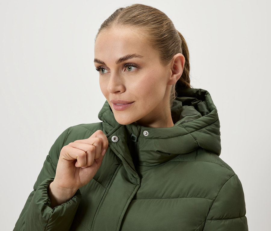 Frau schließt eine olivgrüne Steppjacke mit Kapuze.