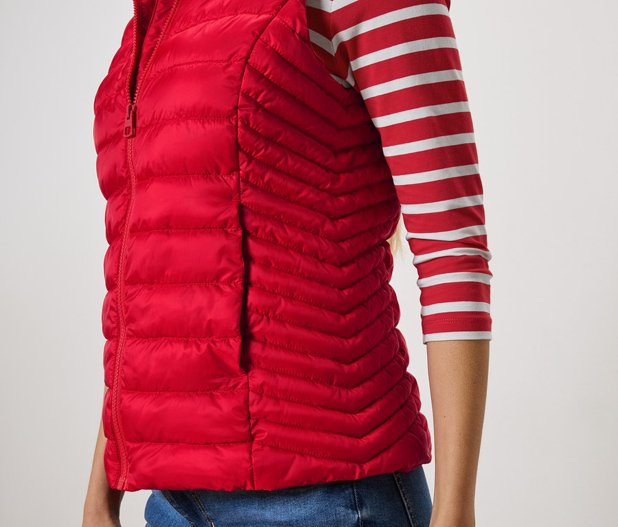 Nahaufnahme einer Frau, die eine rote Steppweste und ein gestreiftes Hemd trägt.