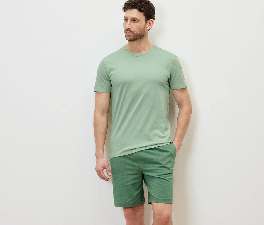 Mann posiert in einem grünen 3 T-Shirts mit Rundhalsausschnitt und grünen Shorts.