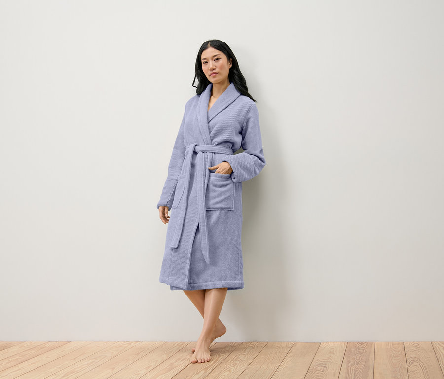 Eine Frau steht und trägt einen hellvioletten Bademantel.