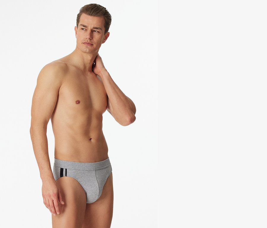 Mann posiert barfuß in 3 SCHIESSER Slips, grau meliert, mit schwarzen Streifen an der Seite.