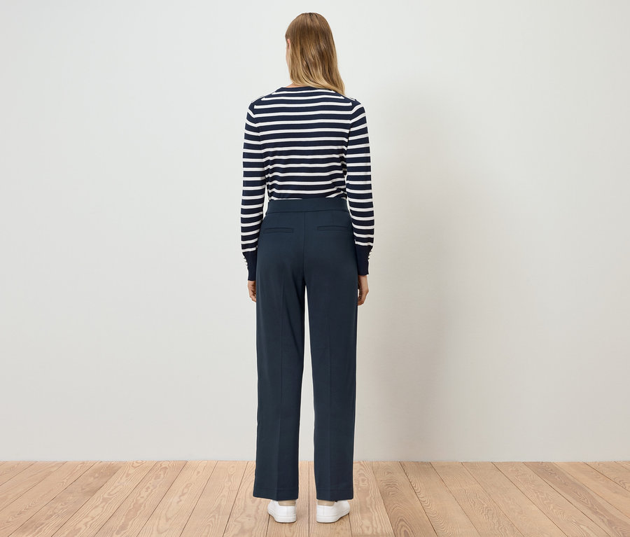 Eine Frau steht mit dem Rücken zur Kamera und trägt eine blaue Hose und ein gestreiftes Oberteil.