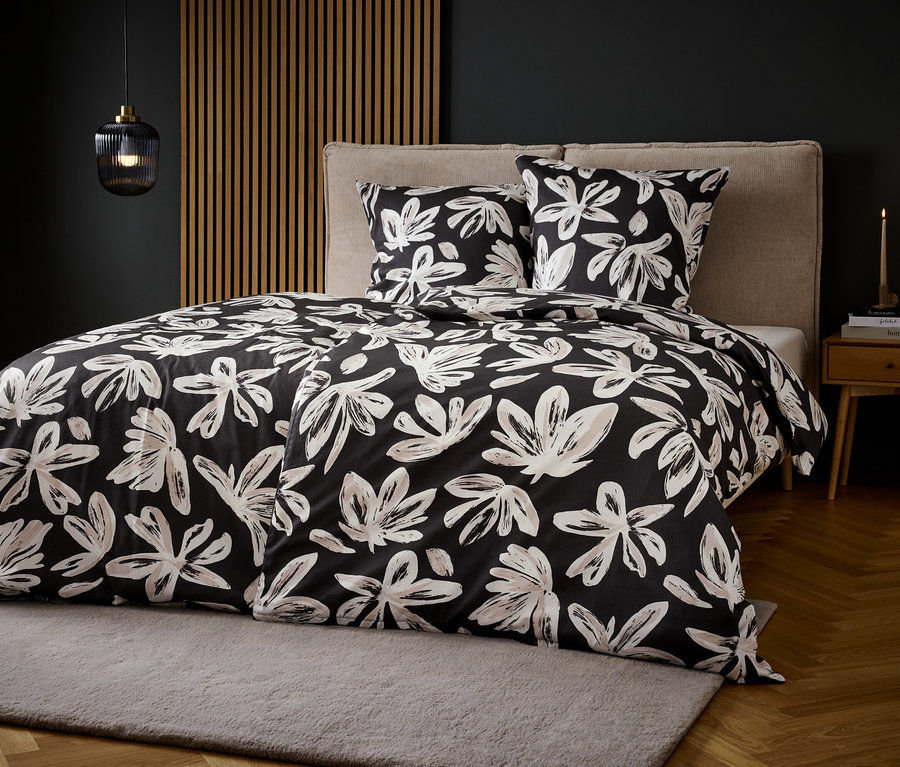 Bett mit schwarz-weißem Blumenmuster-Bettzeug auf grauem Teppich.
