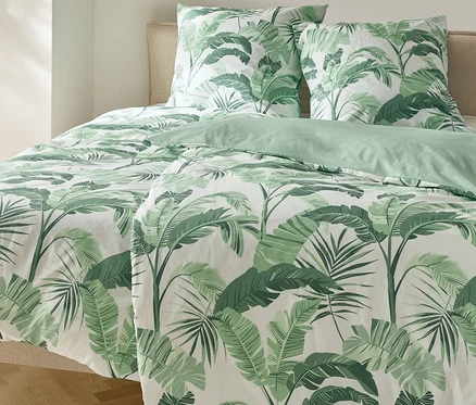 Bett mit Renforcé-Bettwäsche, Palmenmuster und zwei Kissen.