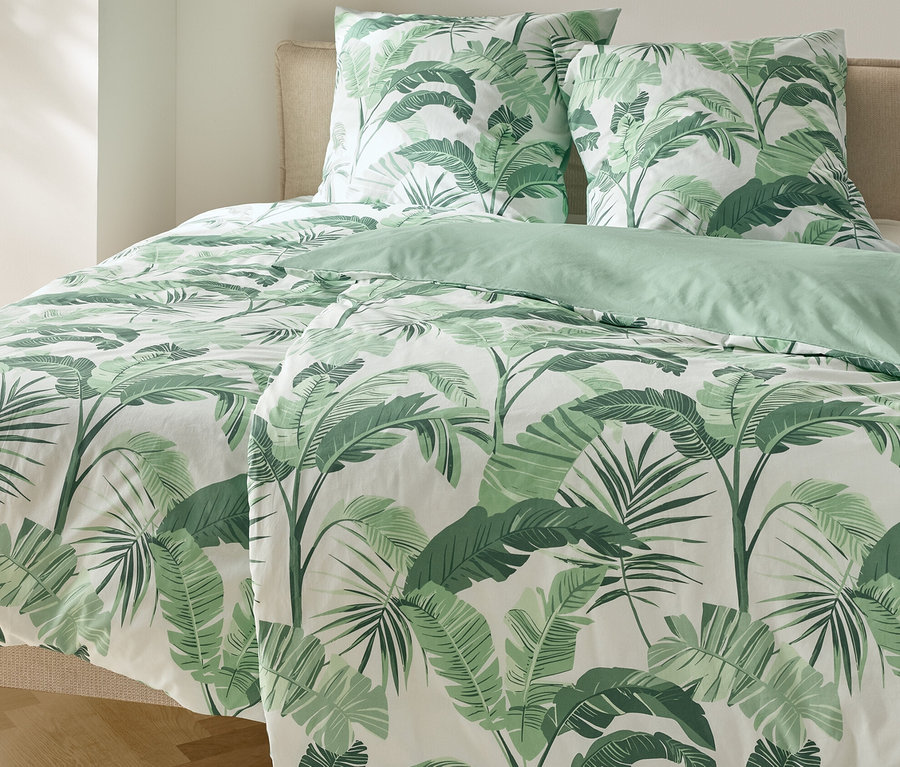 Bett mit Renforcé-Bettwäsche, Palmenmuster und zwei Kissen.