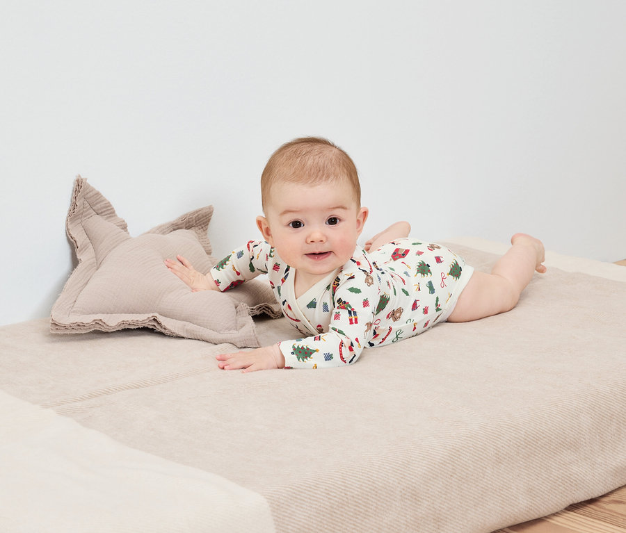Baby liegt auf dem Bauch auf einer Decke neben einem sternförmigen Kissen.