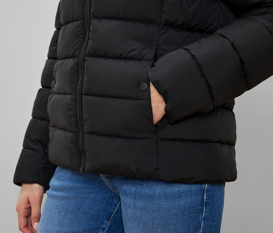 Person in schwarzer Steppjacke mit Hand in der Tasche und blauen Jeans.