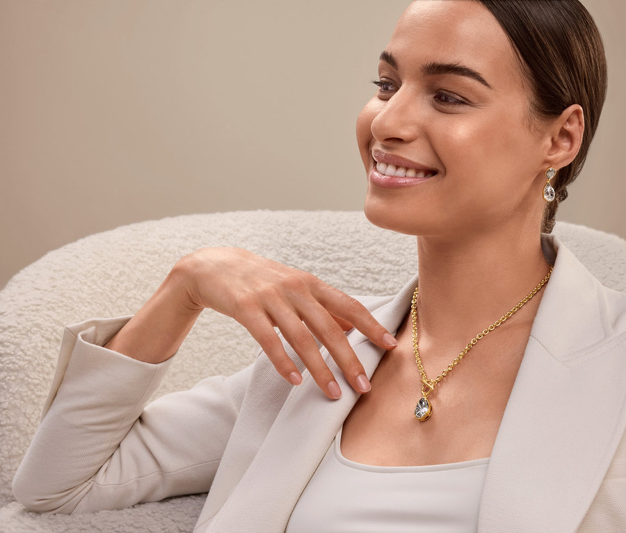 Frau sitzt und trägt eine goldene Halskette und Ohrringe.
