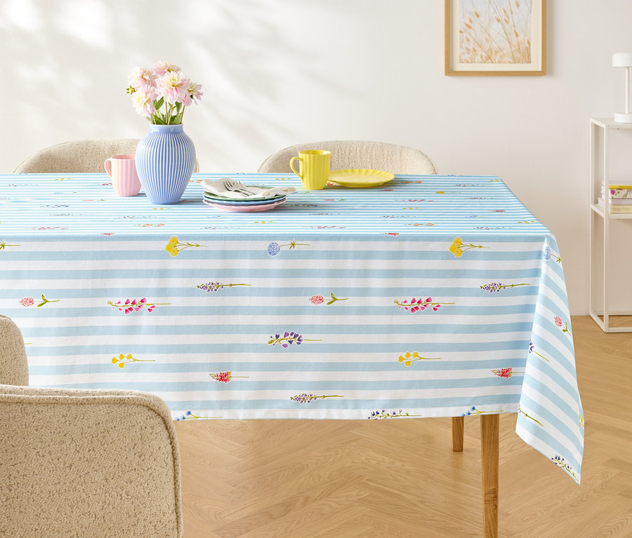 Esstisch mit blau-weiß gestreifter Tischdecke, darauf Geschirr, Besteck und eine Vase mit Blumen.