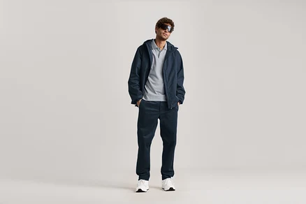 Ein Mann steht mit Sonnenbrille, marineblauer Jacke und marineblauer Chino.