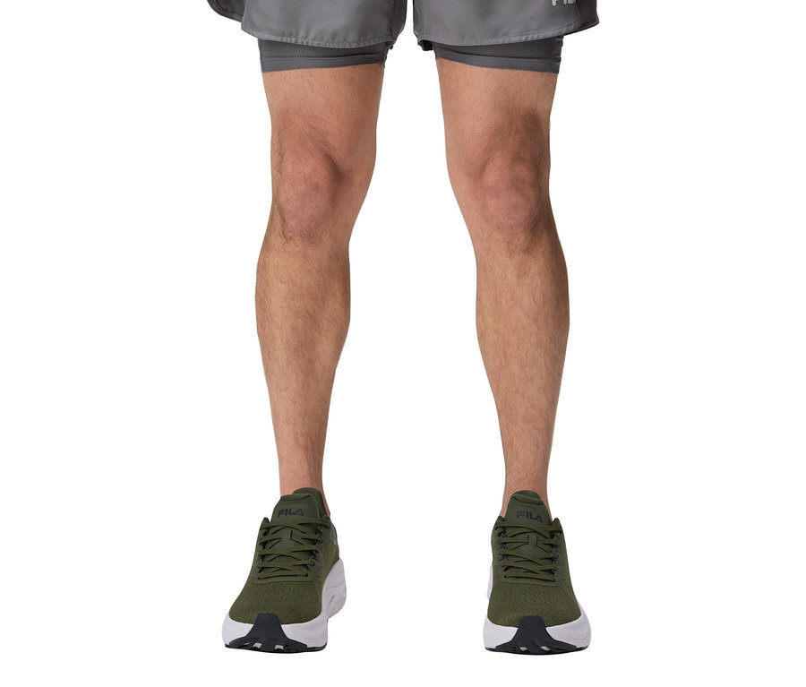 Beine einer Person, die FILA Herren-Funktionsshorts und grüne Turnschuhe trägt.