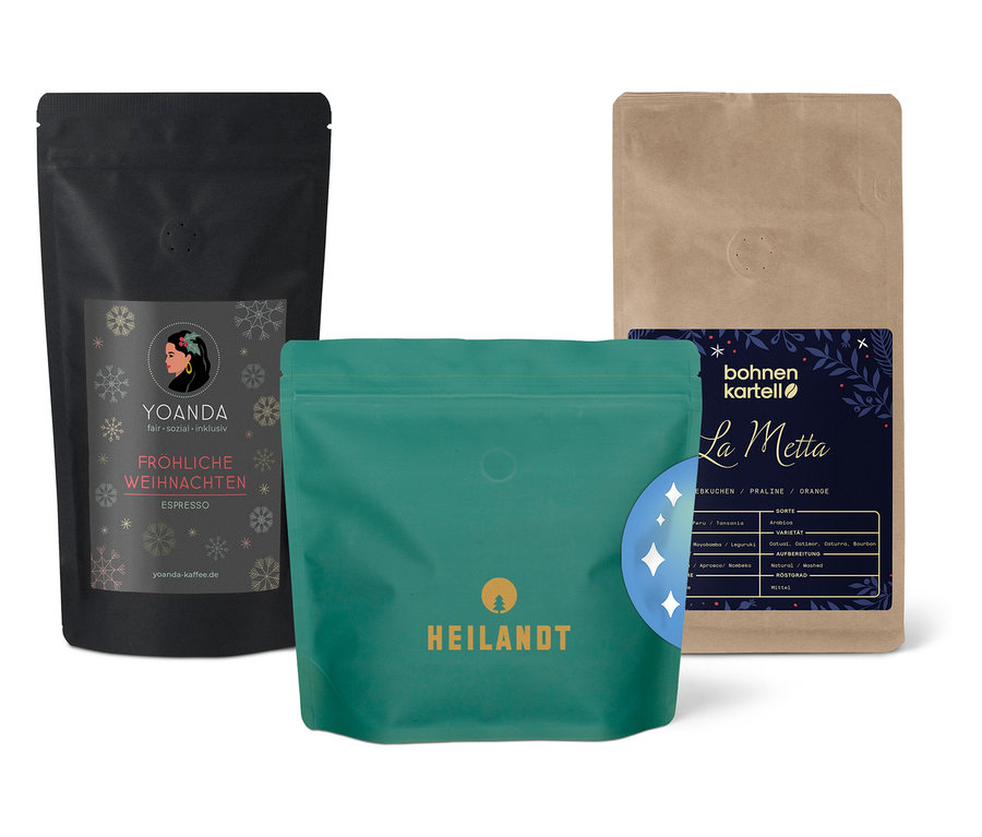 Drei Kaffeepackungen unterschiedlicher Marken stehen nebeneinander. Eine Packung ist schwarz mit Schneeflocken, eine ist grün und eine ist beige.