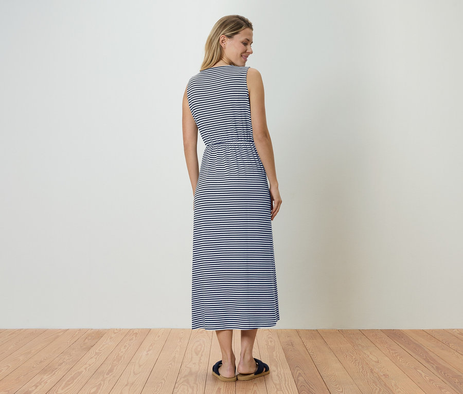 Frau von hinten in blau-weiß gestreiftem, ärmellosem Maxikleid und Sandalen.