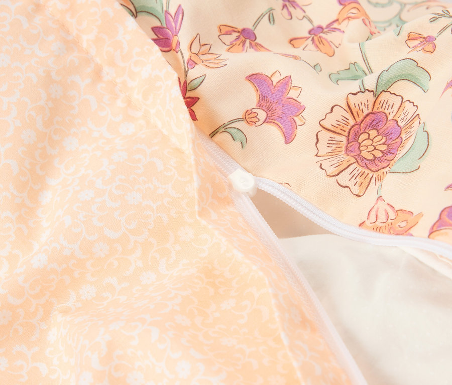Nahaufnahme eines Kissens mit Reißverschluss. Das Kissen hat ein florales Muster in Gelb-, Orange- und Lilatönen.