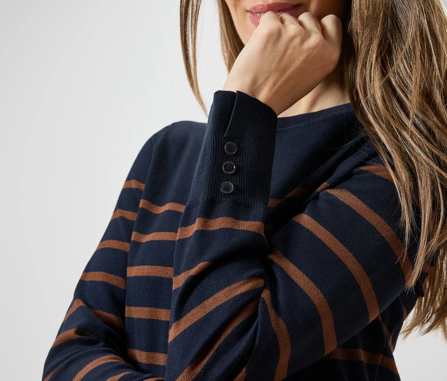 Frau mit blau-braun gestreiftem Pullover, Hand am Kinn. Der Ärmel hat drei Knöpfe.