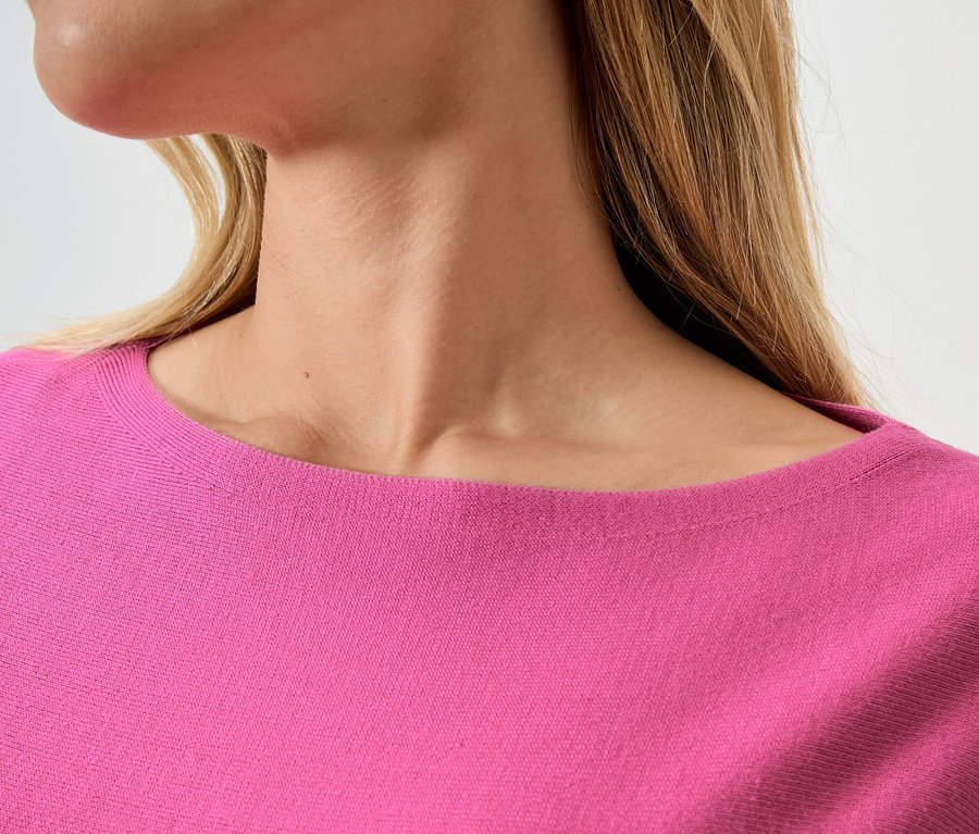 Nahaufnahme einer Frau mit blonden Haaren, die einen pinkfarbenen Pullover trägt.