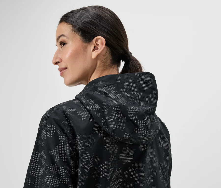 Frau mit Pferdeschwanz, von hinten gesehen, trägt eine schwarze Regenjacke mit Kapuze und Blumenmuster.
