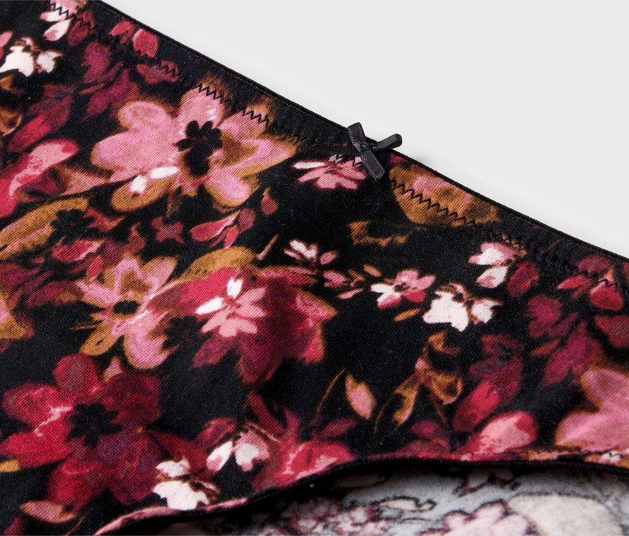 Nahaufnahme eines Slips mit Blumenmuster in Rosa-, Rot- und Brauntönen auf schwarzem Grund, verziert mit einer kleinen Schleife.