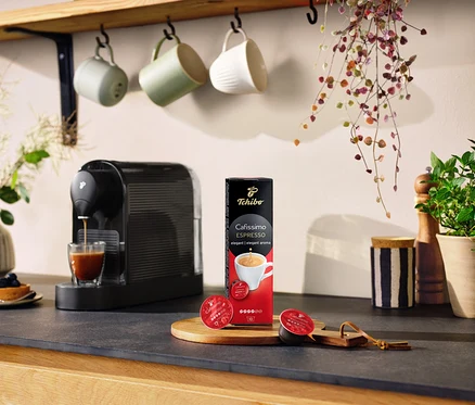 Espressomaschine gießt Kaffee in ein Glas neben einer Packung Cafissimo Espresso elegant - 10 Kapseln.