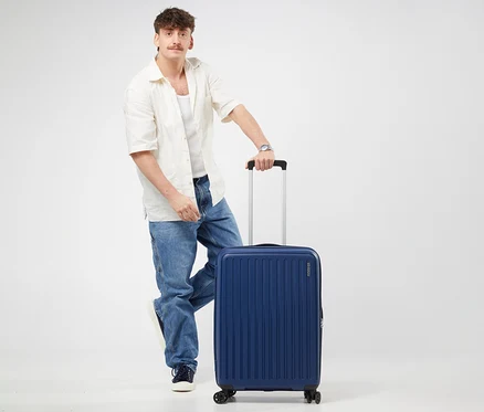 Ein Mann steht mit einem Fuß auf einem mittelgroßen American Tourister Rejoy Spinner Koffer in Navy Blue und hält dessen Griff.