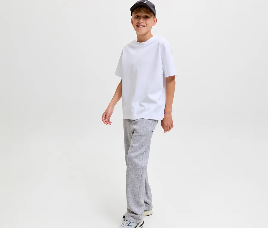 Lächelnder Junge trägt ein weißes T-Shirt, eine dunkle Baseballkappe und graue Jack&Jones Bradley Sweatpants.