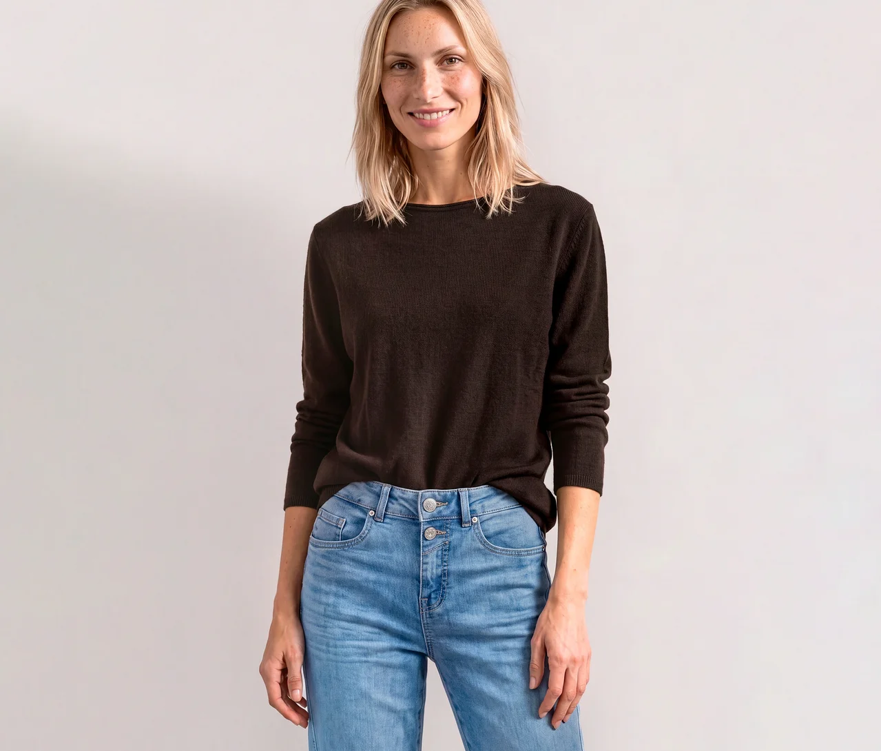 Lächelnde Frau trägt einen braunen Street One Strickpullover und helle Jeans.