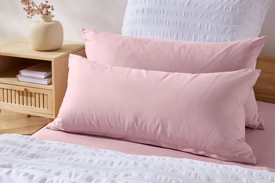 Zwei rosa Microfaser-Kopfkissenbezüge (ca. 80 x 40 cm) liegen auf einem Bett mit weißer Tagesdecke.