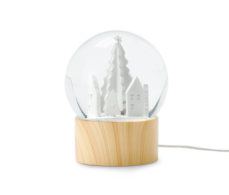 Eine LED-Schneekugel mit weißen Häusern und Bäumen auf einem Holzsockel.