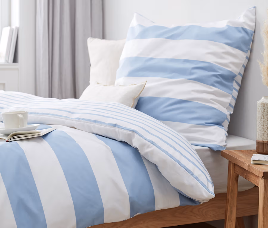 Blau gestreifte Microfaser-Bettwäsche (Normalgröße und Übergröße) auf einem Bett mit Buch und Tasse.