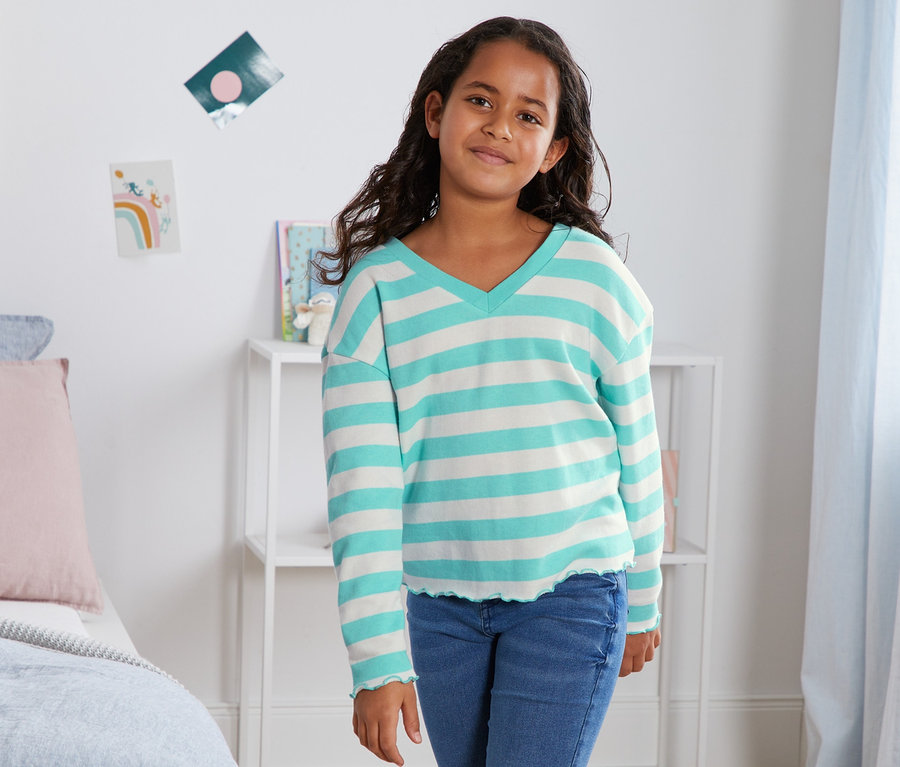 Mädchen posiert in einem blau gestreiften Sweatshirt aus Bio-Baumwolle.