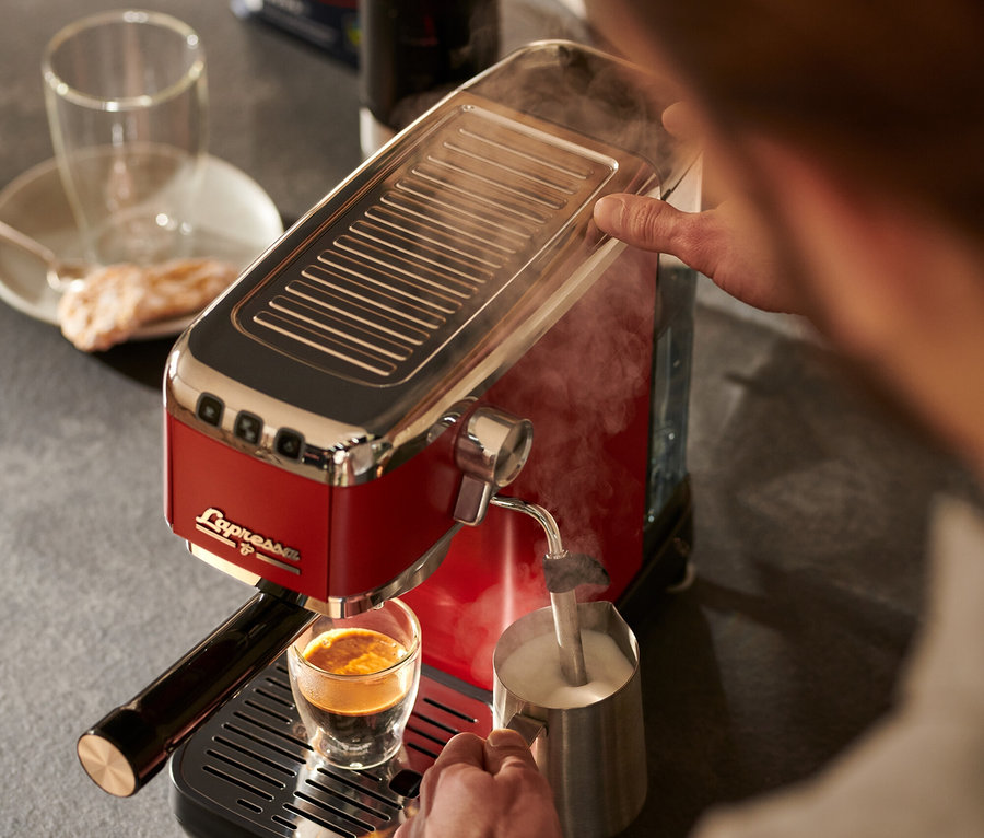 Ein Mann bereitet mit einer roten »Lapressa« Siebträgermaschine Kaffee zu und schäumt Milch auf.