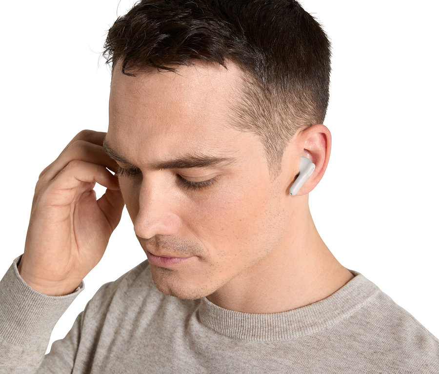 Mann mit hellbraunem Pullover justiert TWS-In-Ear-Kopfhörer im Ohr.
