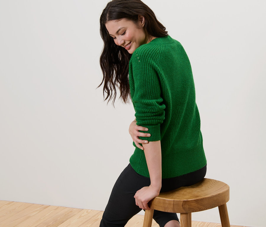 Frau sitzt auf Hocker und trägt grünen Strickpullover.