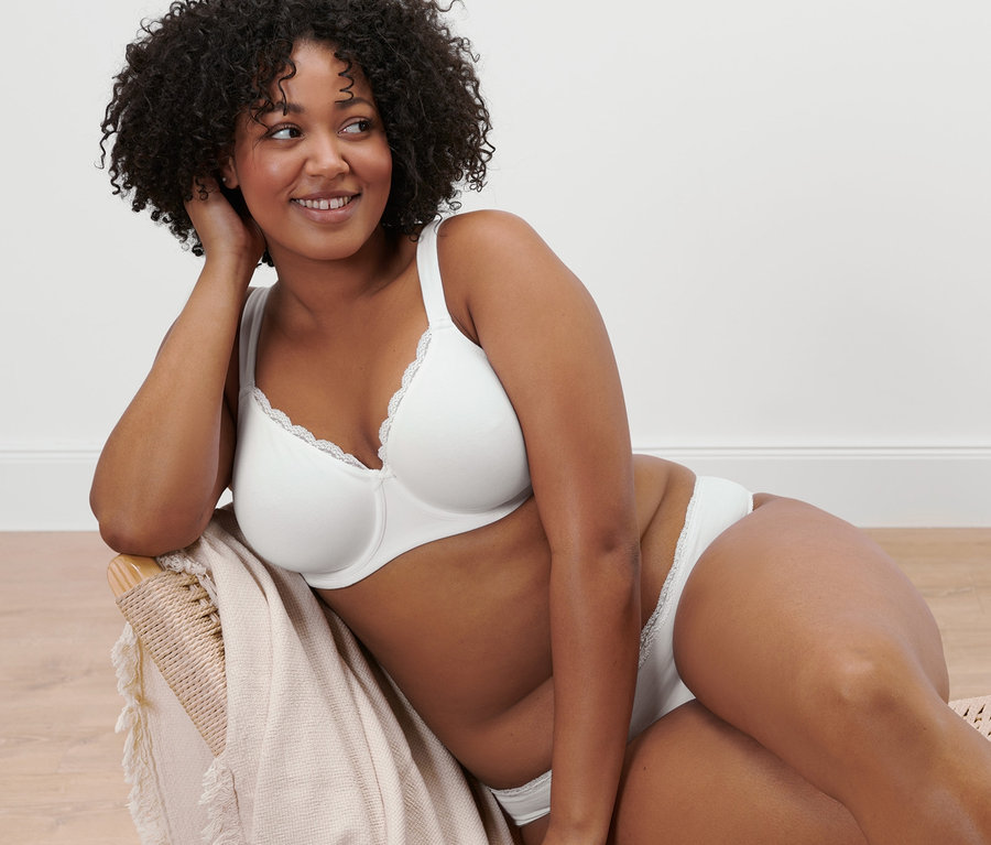 Frau sitzt im Sessel und trägt einen weißen Bügel-BH.