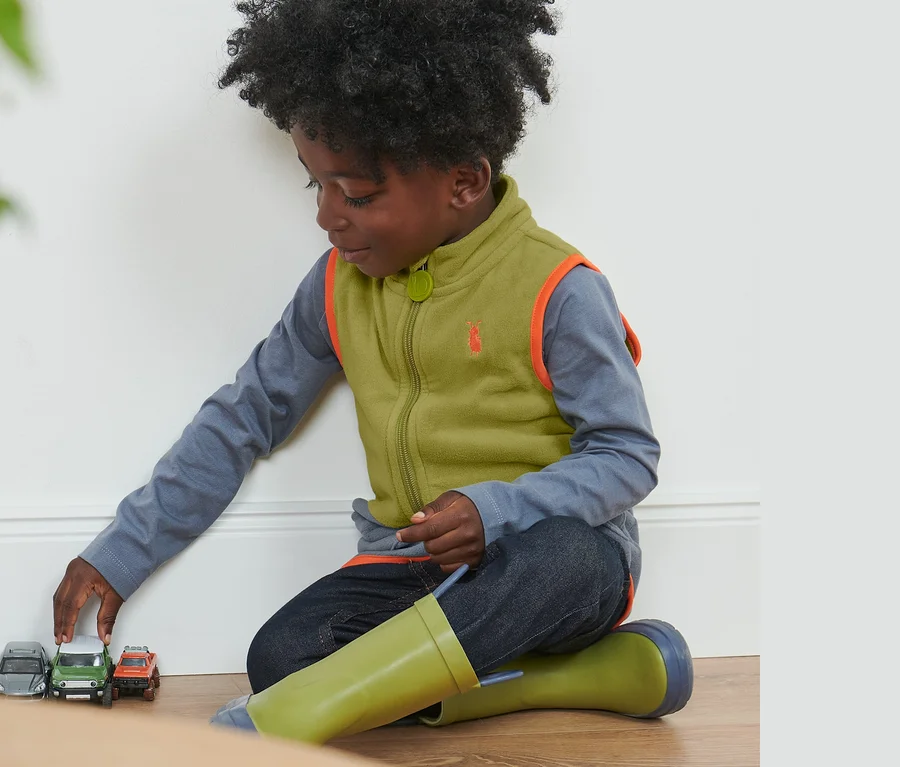 Ein Junge spielt mit Spielzeugautos auf dem Boden und trägt eine Kleinkinder-Fleeceweste im Colorblocking-Design.