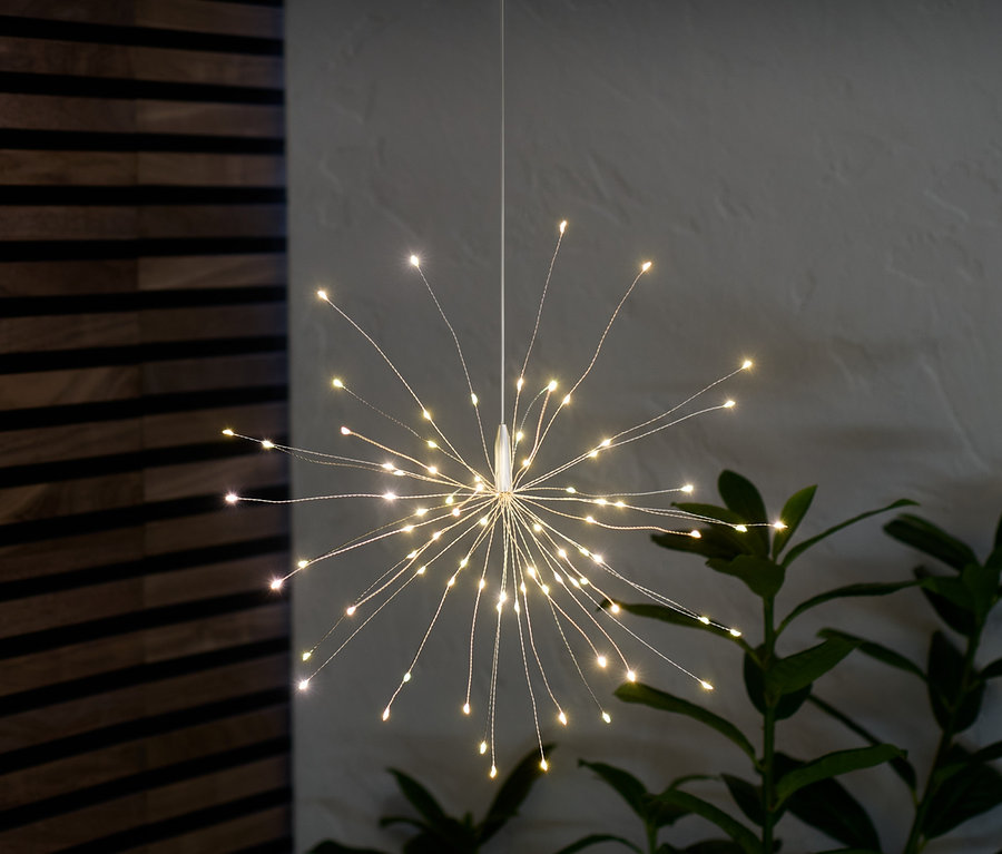 Ein LED-Leuchtzweig hängt und leuchtet im Raum neben einer Pflanze.