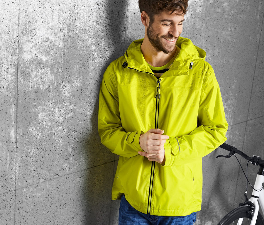 Mann lehnt an Wand, trägt gelbe Regenjacke.