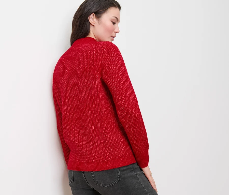 Frau trägt einen roten Grobstrickpullover mit Zopfmuster und graue Jeans.