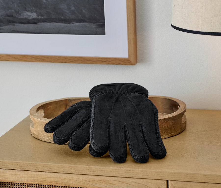 Schwarze Handschuhe liegen auf einem Holztablett auf einem Schrank neben einer Lampe.