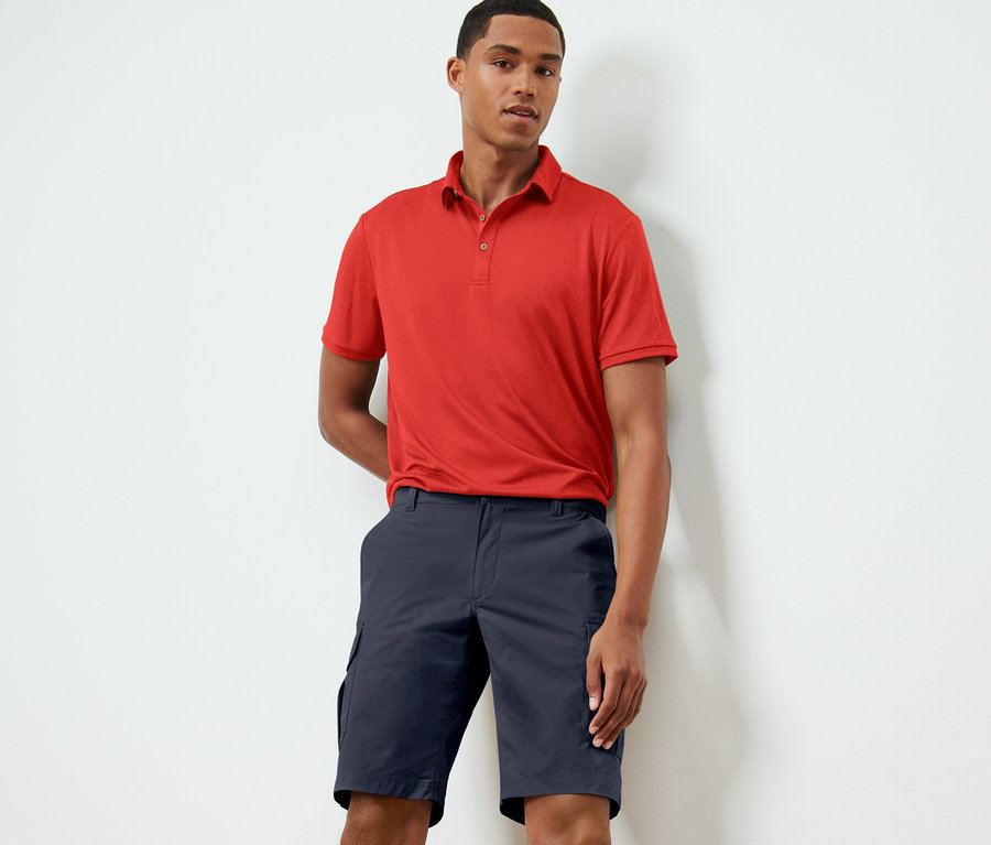 Mann posiert in rotem Polohemd und blauen Funktionsshorts.